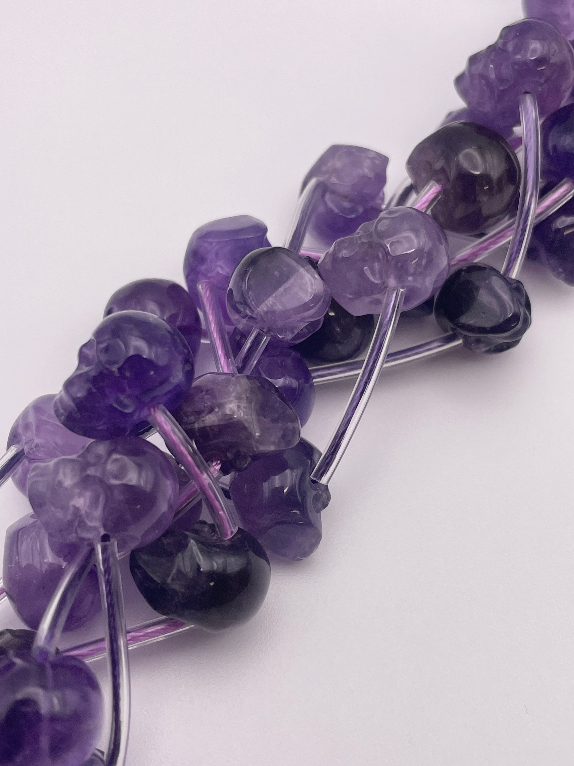 Close-up image of a beaded necklace featuring 10mm Amethyst Skull Beads and black stones, showcasing their potential healing properties. The beads are strung together on a shiny, flexible wire, creating a detailed and intricate design against a white background—an exquisite addition to any jewelry collection.