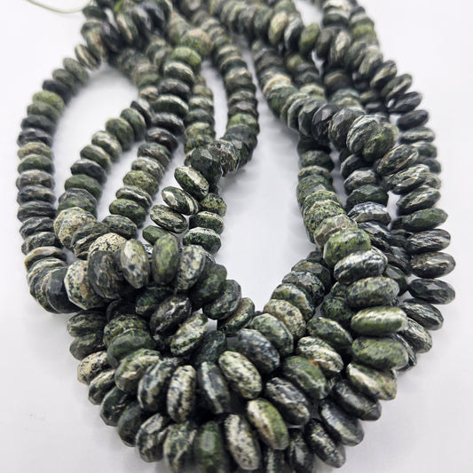 A close-up view highlighting multiple strands of the 10mm Green Jade Rondelle Bead Strand, along with gray marbled stone beads, emphasizes their smooth, rounded shapes and intricate patterns. These strands are artfully arranged in overlapping loops on a white surface.