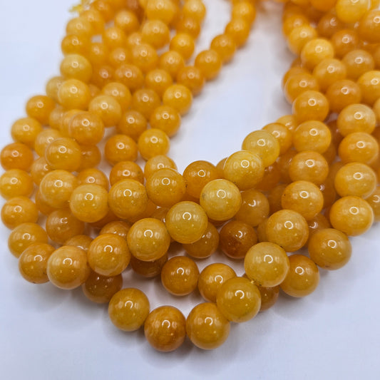 Close-up of multiple strands of lustrous, 10mm round beads from the Yellow Jade Round Bead Strand collection, meticulously arranged on a white surface. These beads showcase a glossy finish and are uniformly shaped to reflect light and exhibit their vibrant hue.