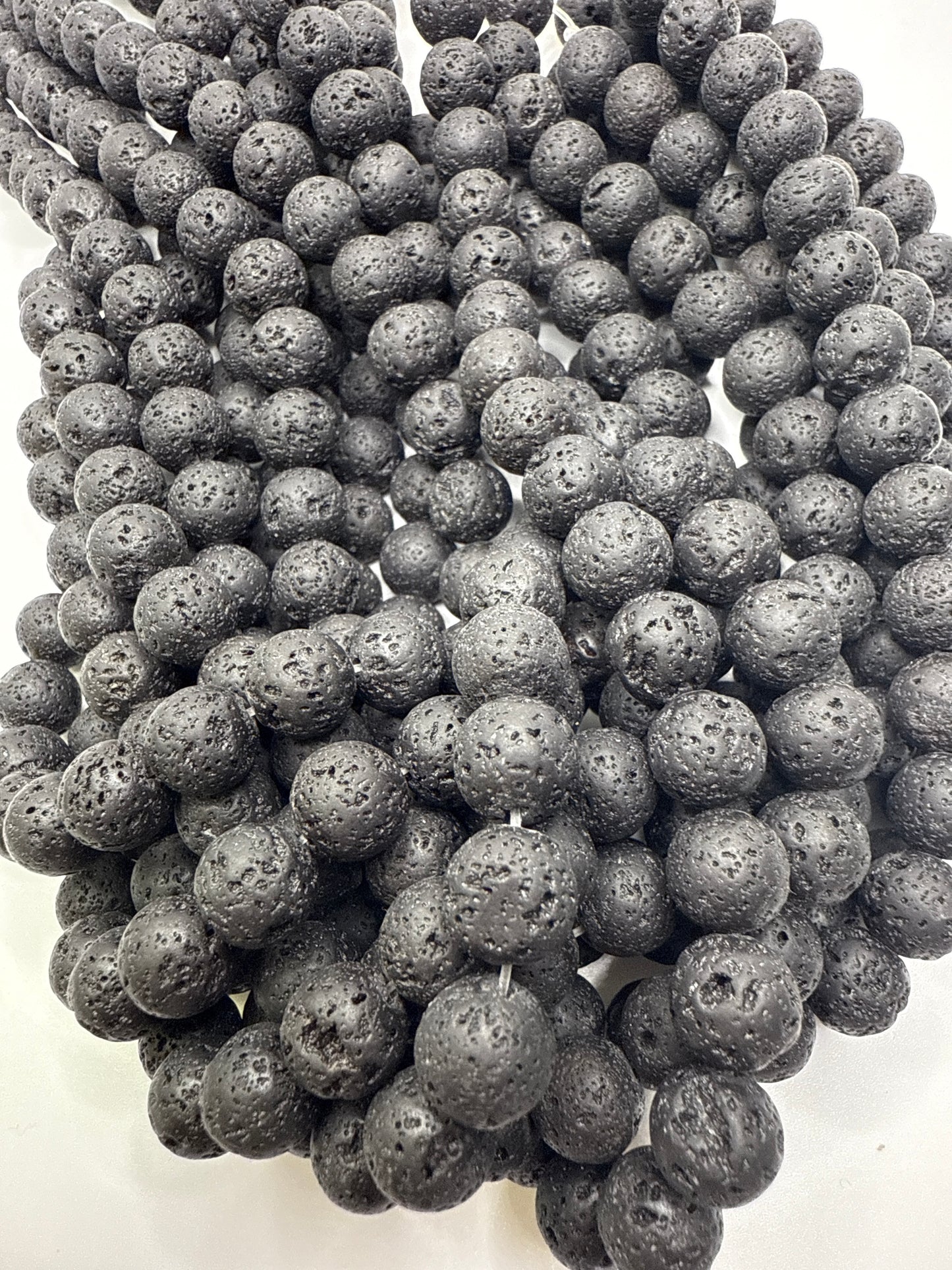 Close-up of dark gray volcanic beads on a white background.10mm Lava Rock Round.