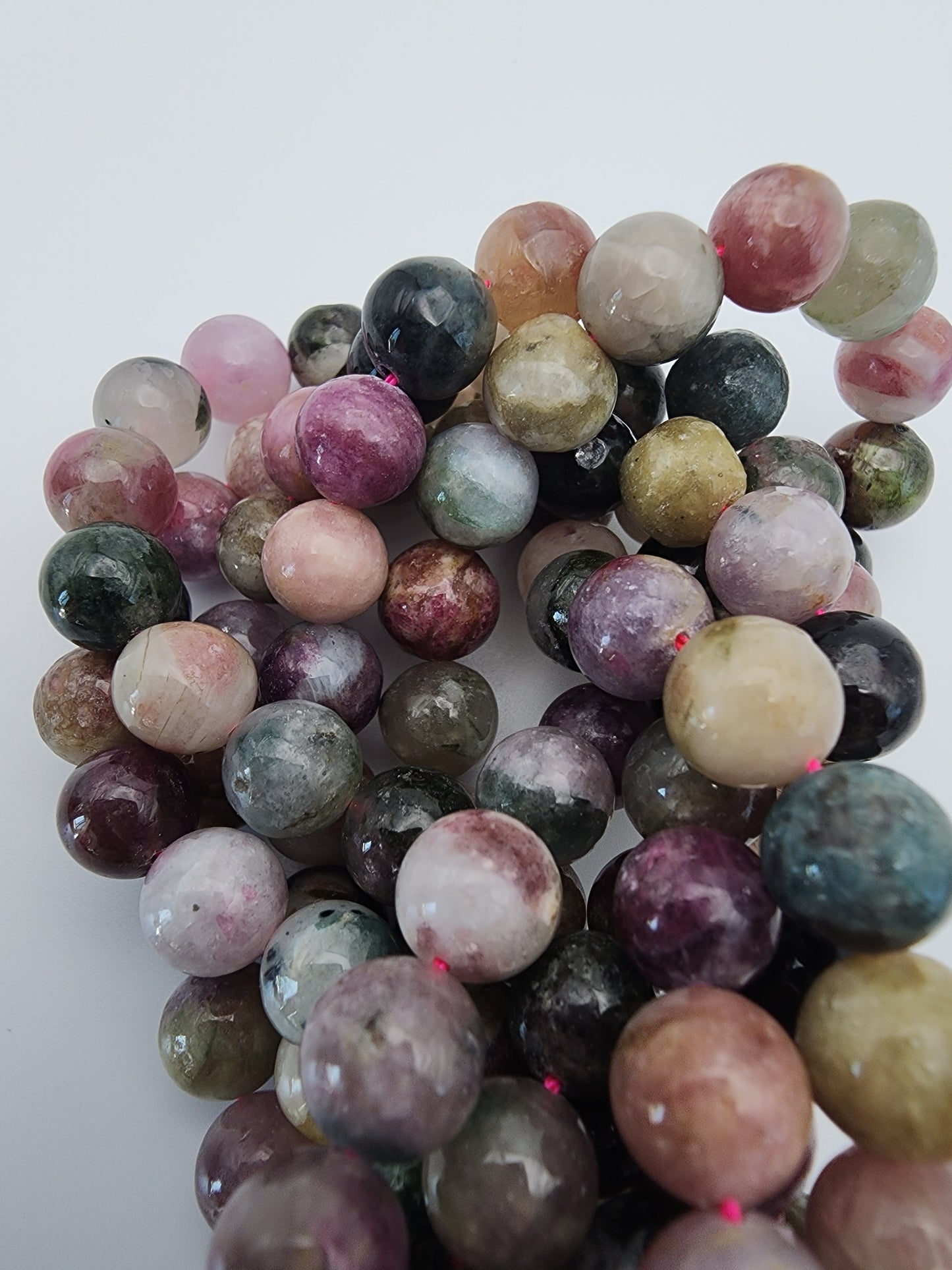 Close-up of multiple strands of 8mm Watermelon Tourmaline Round beads. The beads vary in shades of pink, green, blue, purple, and yellow, with a shiny, reflective surface, and are strung together against a plain white background.