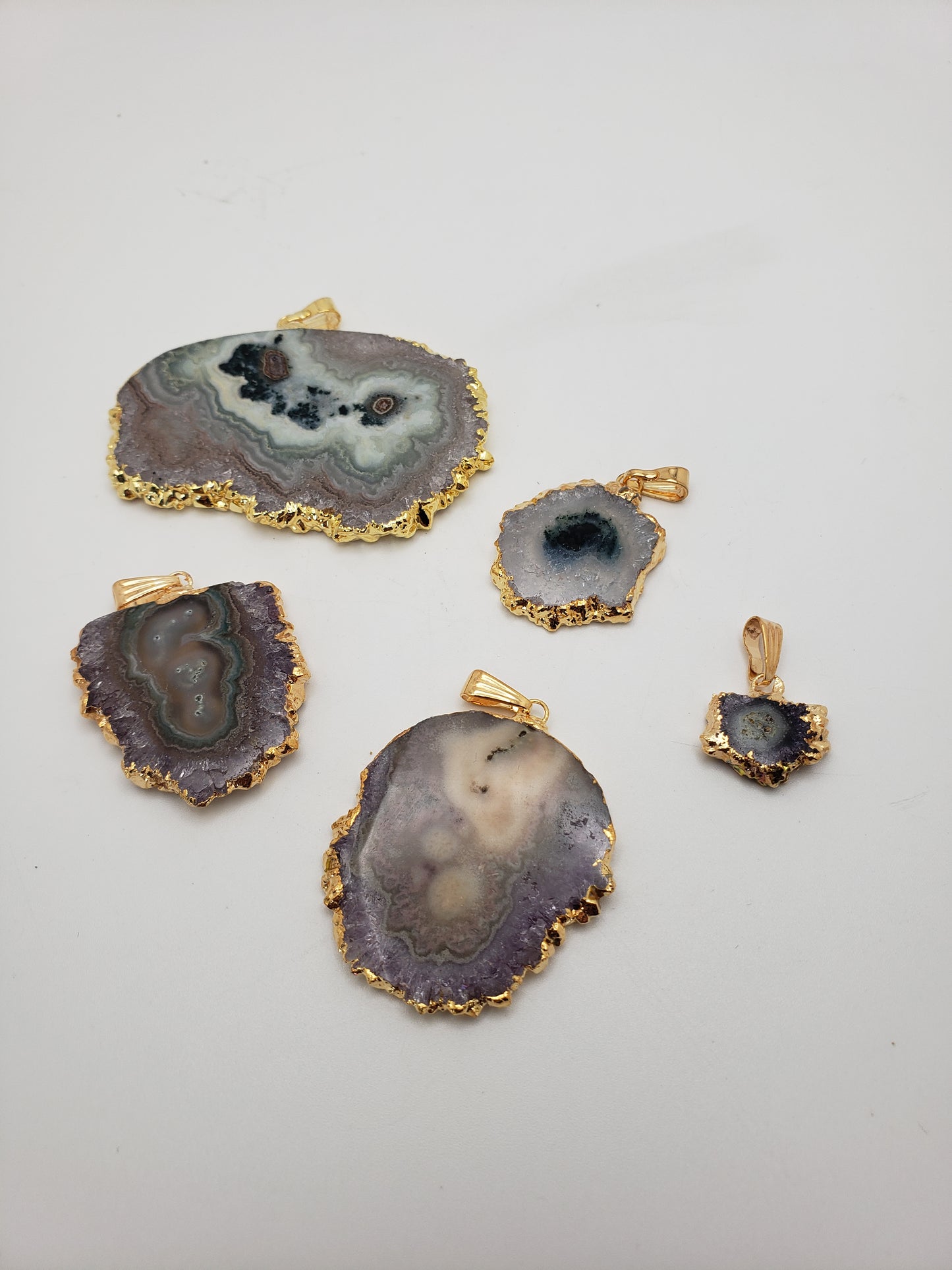 Five GP Stalactite Pendants featuring gold-plated edges are arranged on a white background. Each pendant displays distinct patterns and colors, varying from purple to gray, with differences in size and shape.