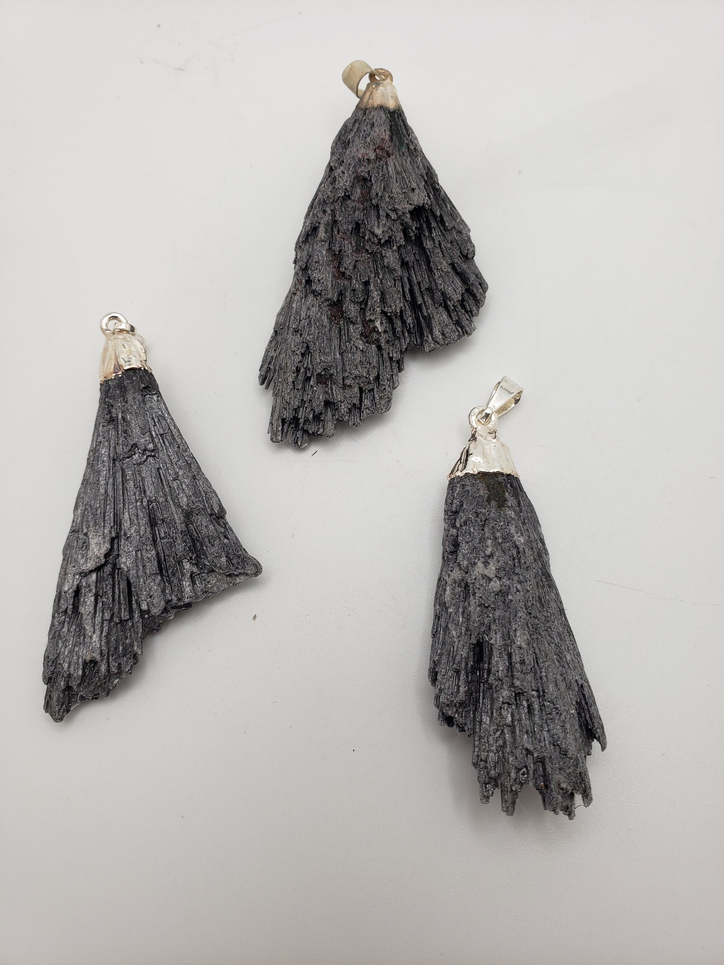 A trio of Black Kyanite Pendants featuring silver bails on a white backdrop, showcasing their fan-like, layered texture.