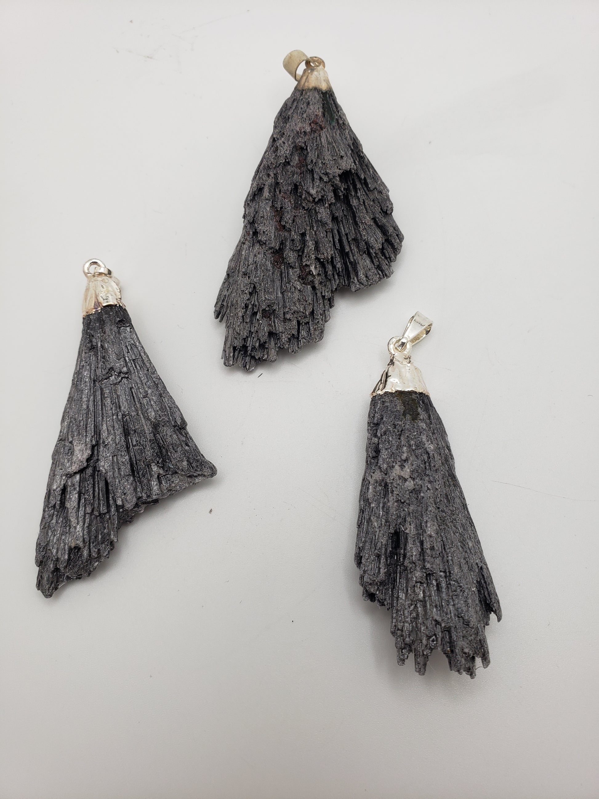 A trio of Black Kyanite Pendants featuring silver bails on a white backdrop, showcasing their fan-like, layered texture.