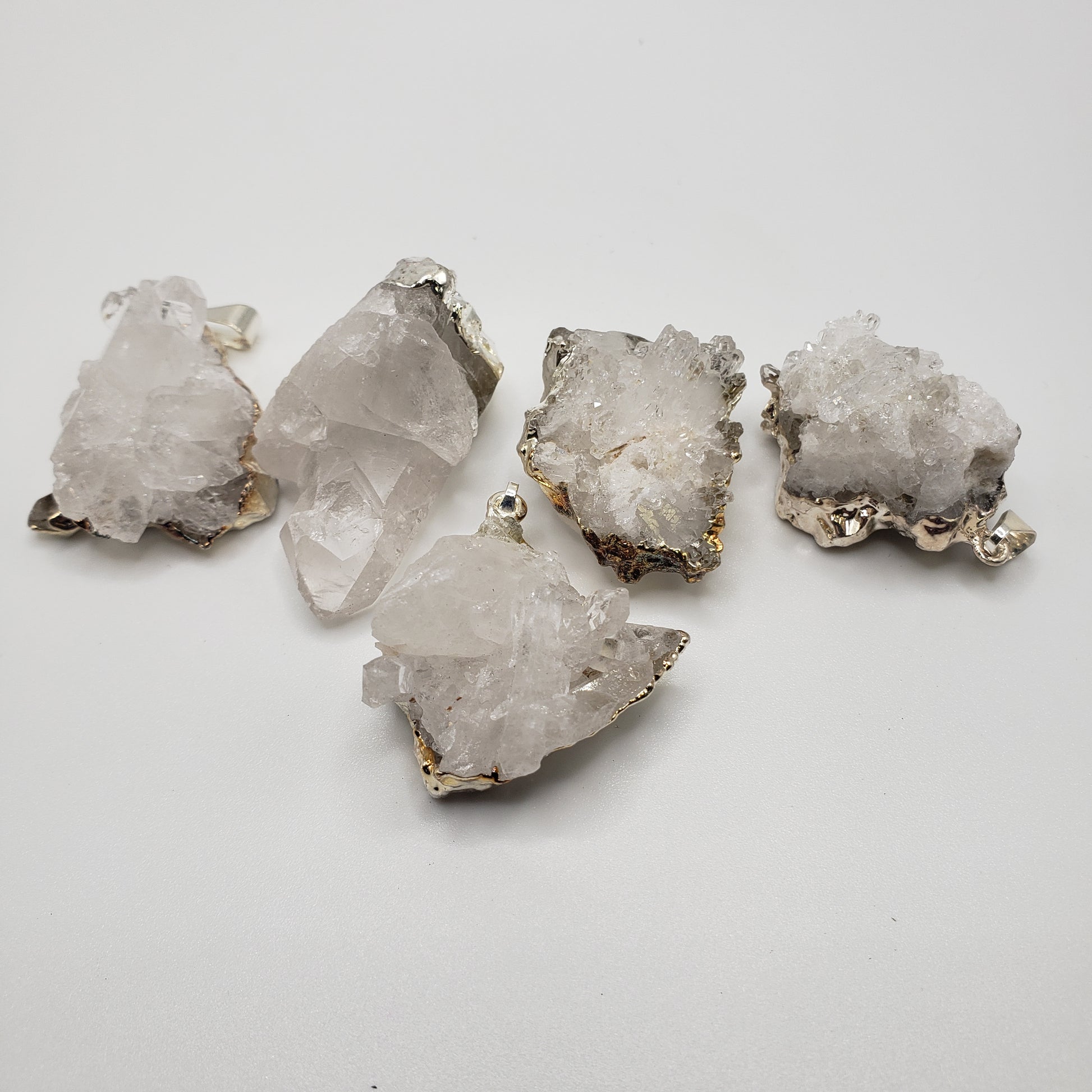 Five rough, translucent white Druizy Quartz Pendant crystals with metallic edges are arranged on a white surface.