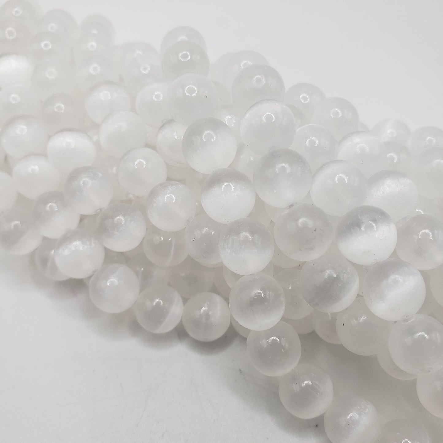A close-up of the 8mm Selenite beads reveals their polished, translucent white surfaces strung together. Each bead has a smooth, glossy finish and is closely arranged, creating a shiny, textured appearance against a white background.