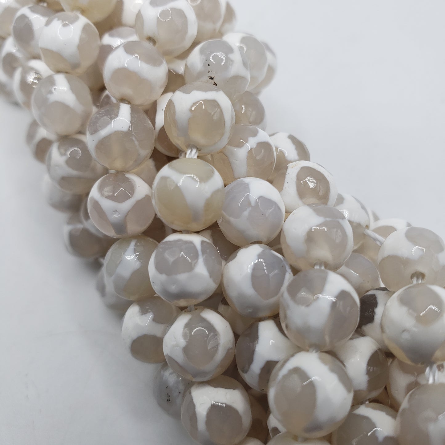 Close-up of strands of glossy, round 8mm White Tibet Agate beads in shades of white, cream, and light brown, tightly arranged on a white background. The beads feature a faceted surface that imparts a subtle shine.