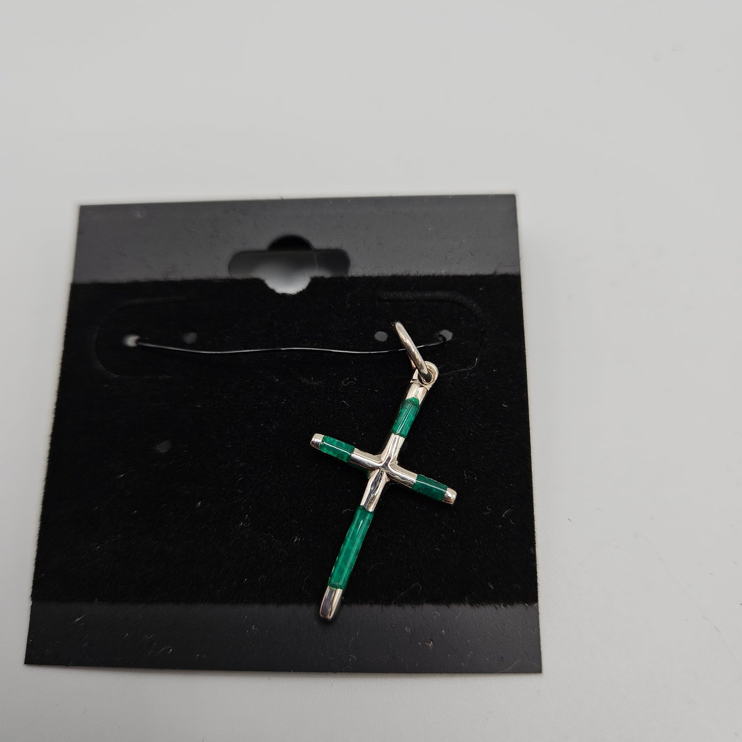 A green and silver cross pendant on a black card with a small silver chain