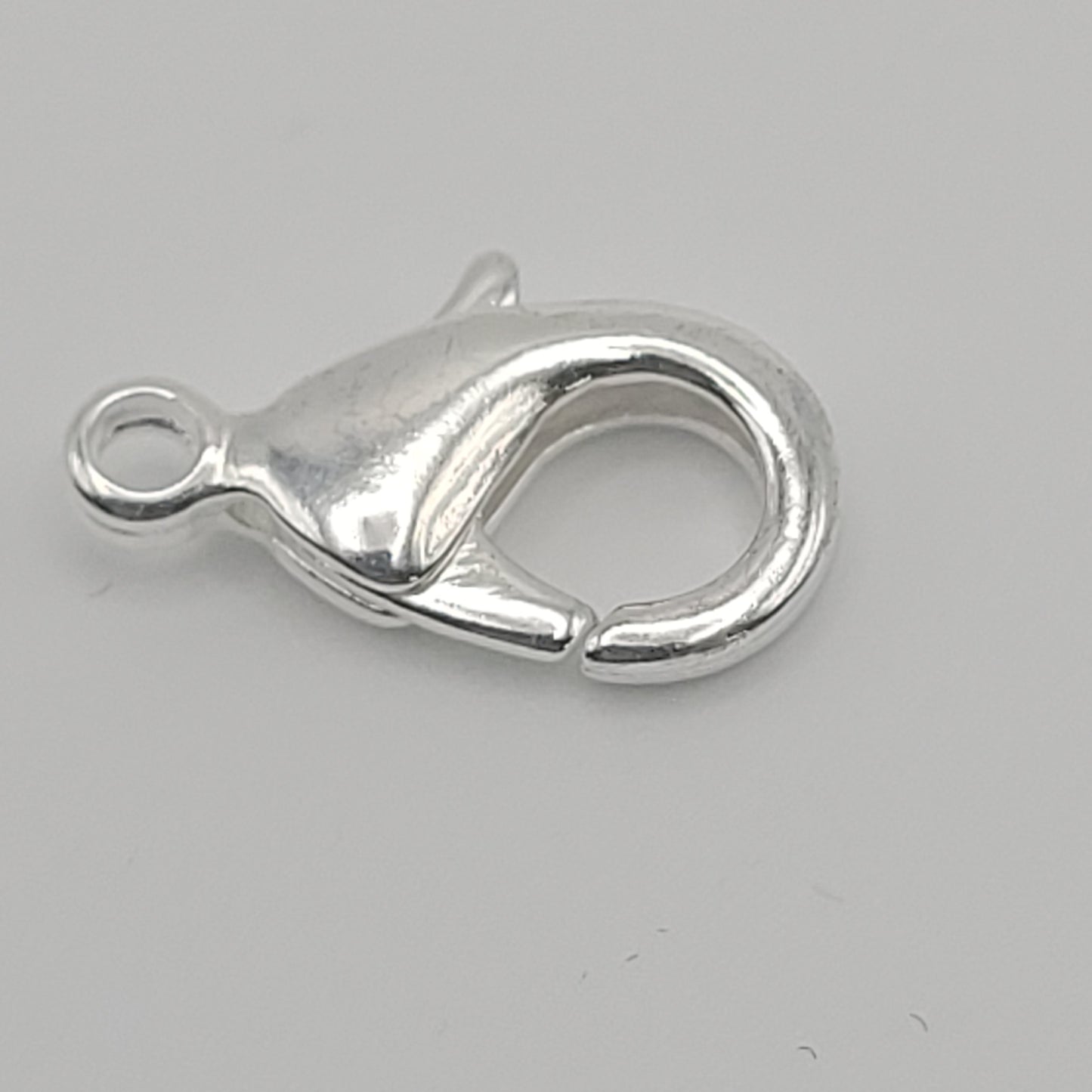 A close-up of the Silver Plated Lobster Claw 15×8mm against a plain background, with the claw open to reveal its curved design and smooth, glistening surface.