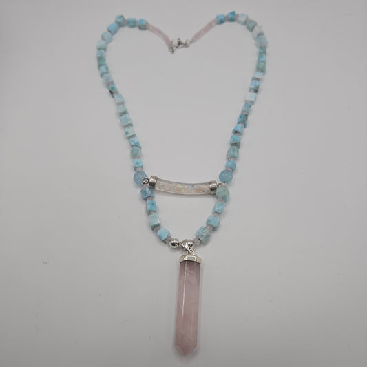 A necklace with a heart-shaped pendant in pink, surrounded by blue beads and a silver chain