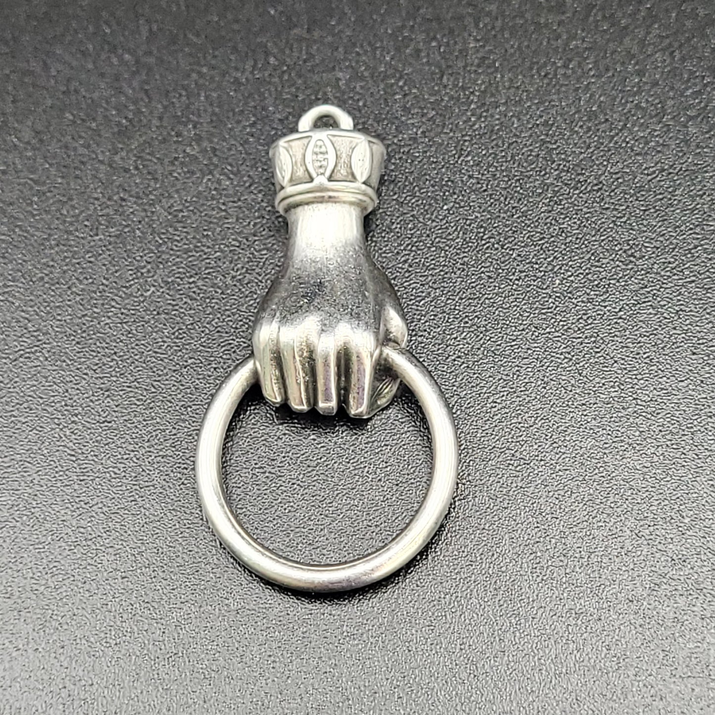 A silver-colored hand wrist ring charm with a small crown on top of the ring