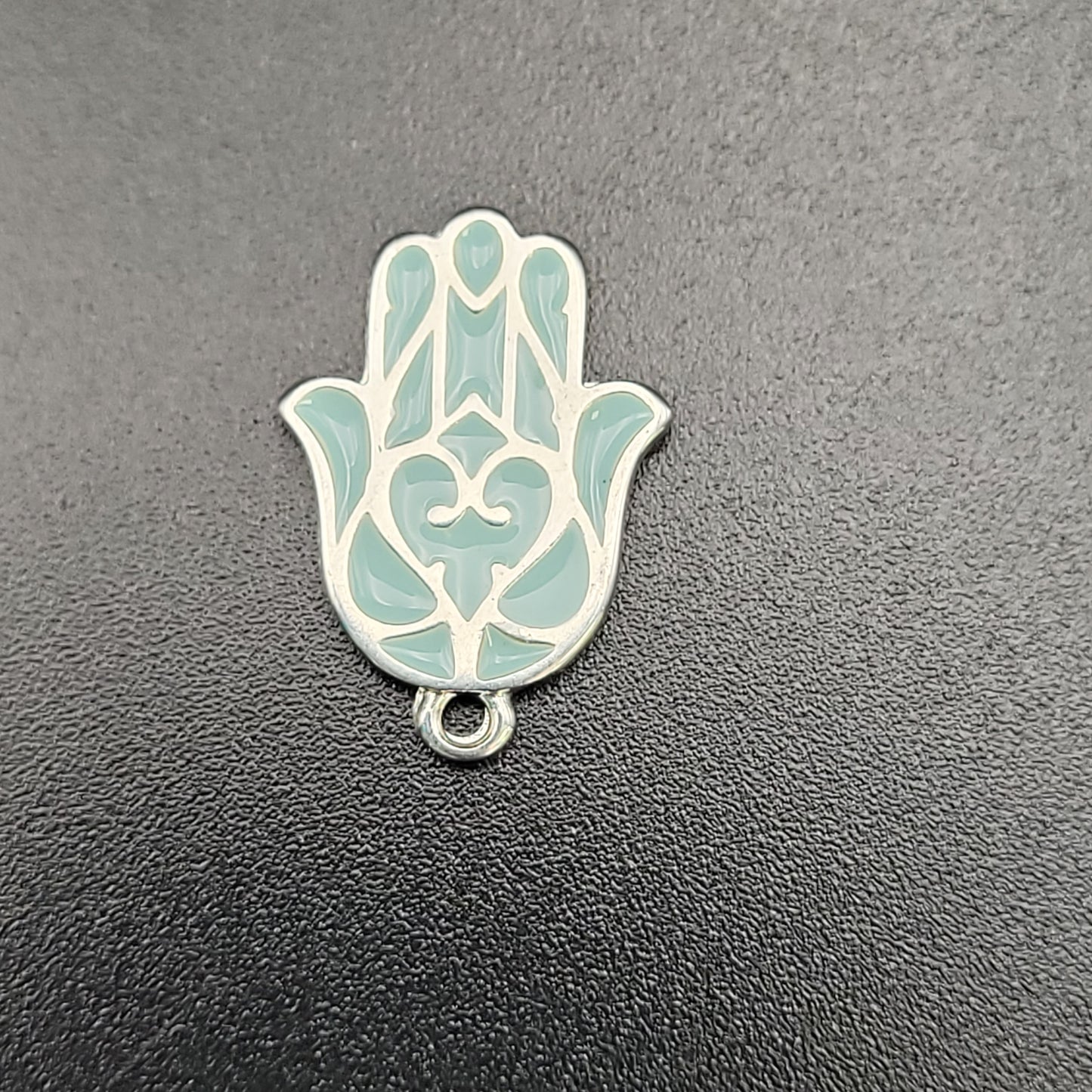 A silver plated blue hamsa charm with a loop on one end