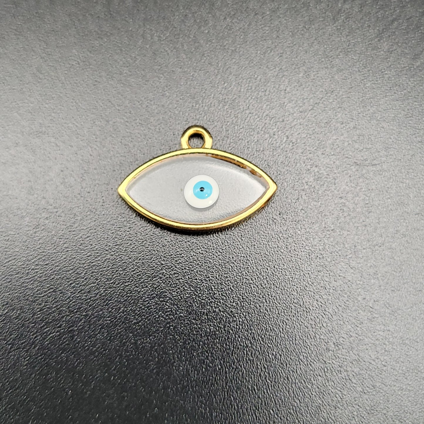 A gold-plated charm in the shape of an eye with a clear and blue enamel design