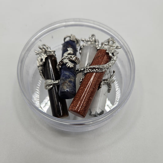 Four Dragon Cylinder Gemstone Pendants, available in a variety of vibrant colors, are elegantly showcased in a round, transparent container. Each exquisite pendant is intricately adorned with a detailed silver dragon design.