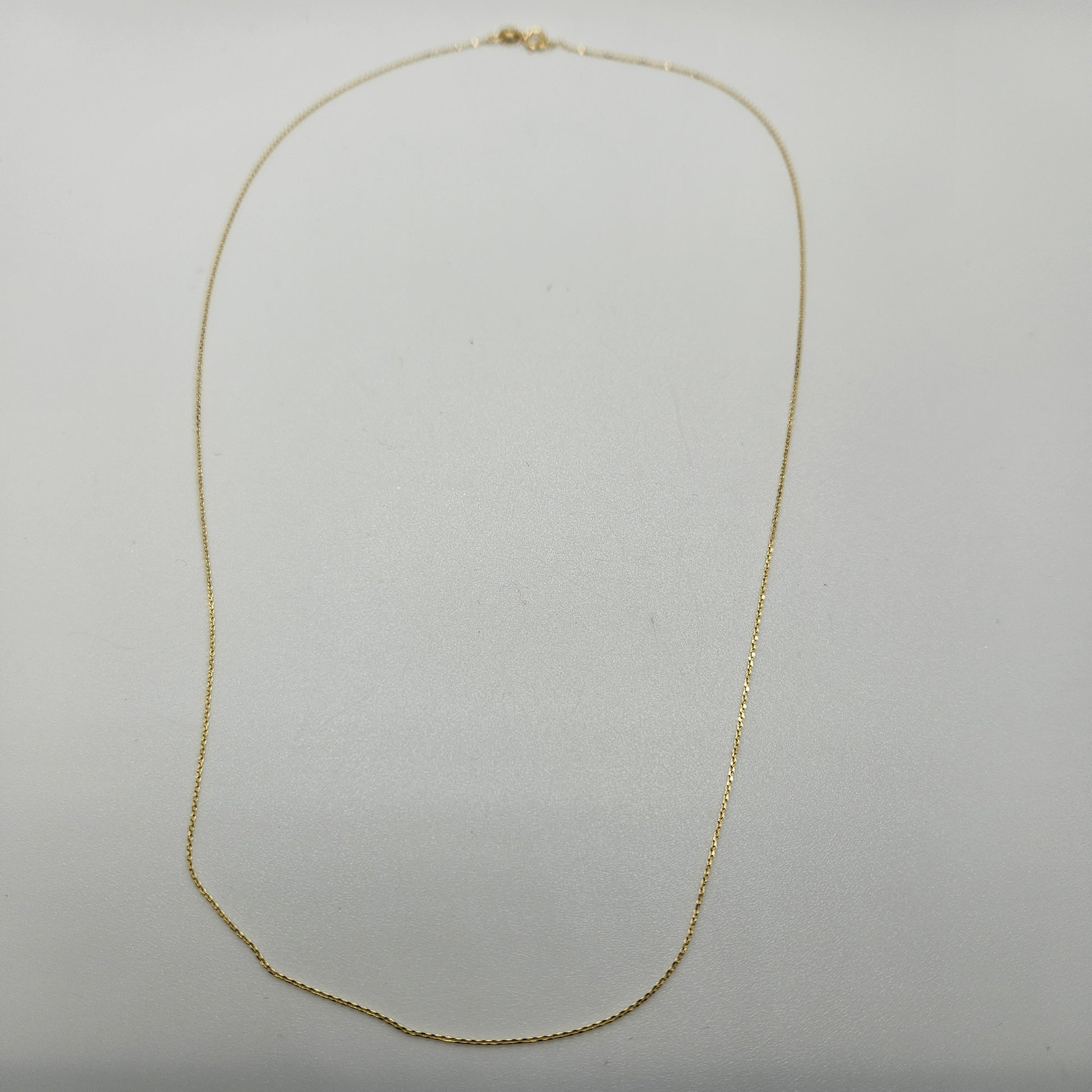 An 18" Fine Gold Cable Chain necklace delicately displayed against a plain white background, featuring a thin chain forming a gentle oval shape.