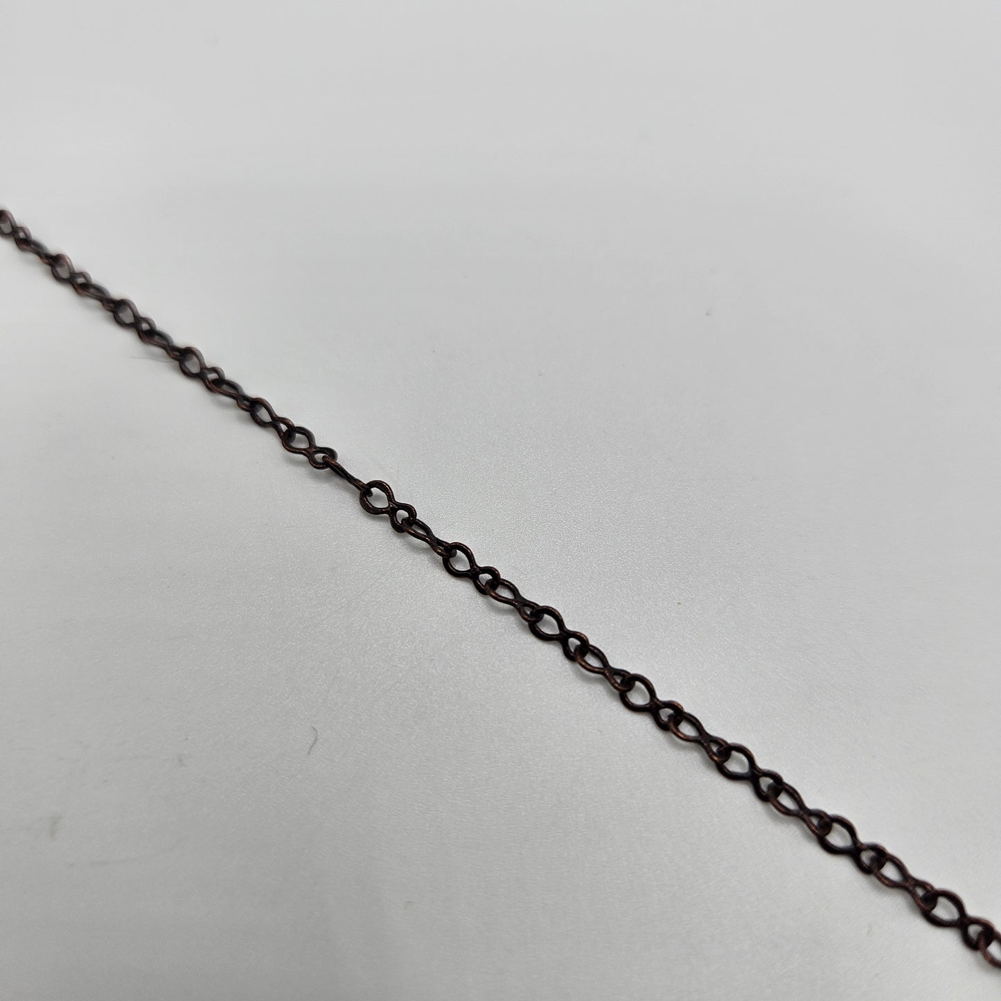 A close-up image of an antique copper fine teardrop chain against a white background.