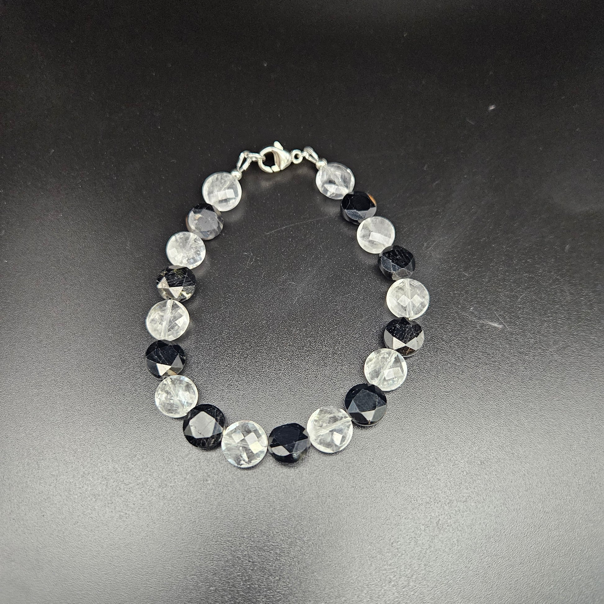 A black tourmaline and clear quartz coin bracelet with a silver-colored chain,