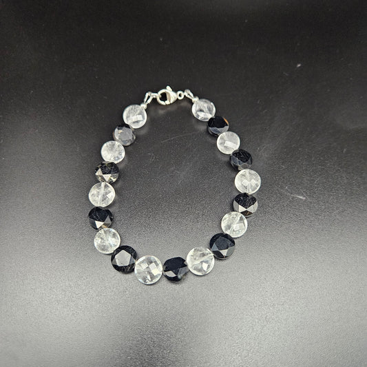 A black tourmaline and clear quartz coin bracelet with a silver-colored chain,