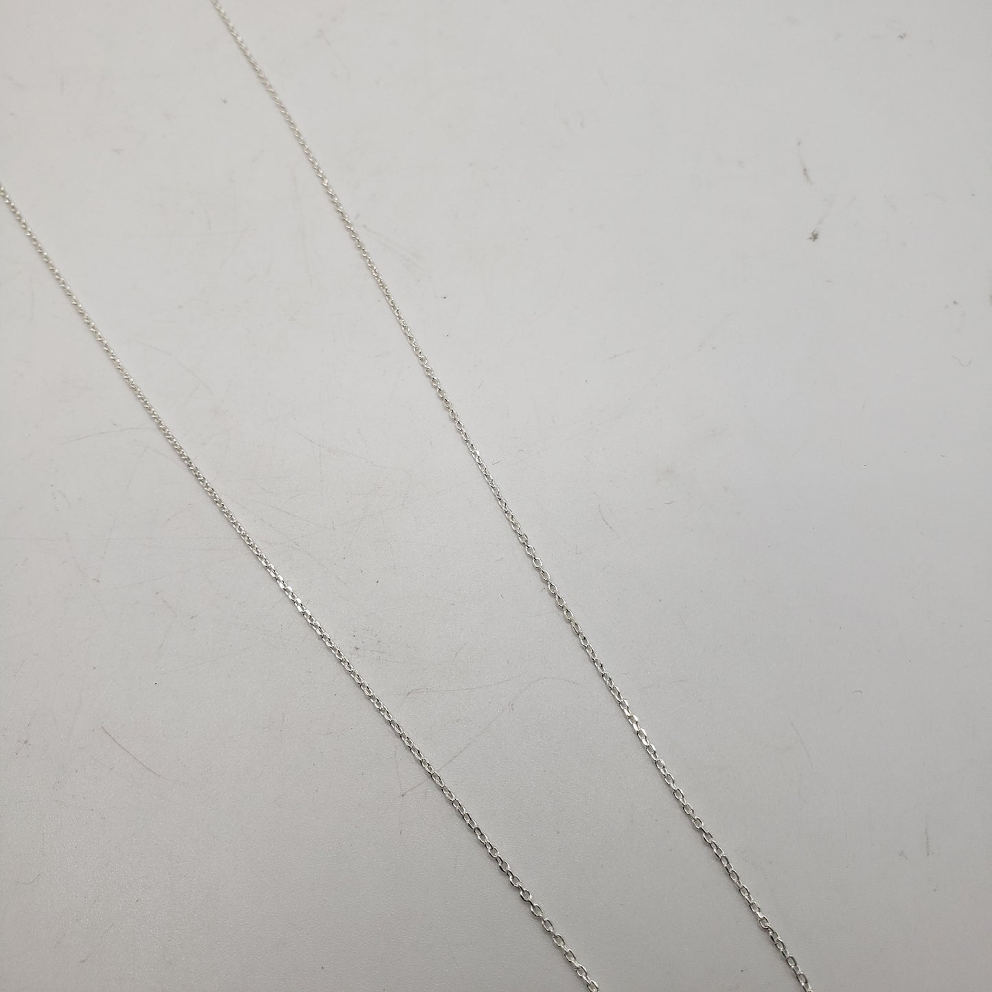 The 20 inch Sterling Silver Link Chain is elegantly displayed against a simple, light-colored background. Its fine link pattern runs diagonally across the image, exuding simplicity and grace.