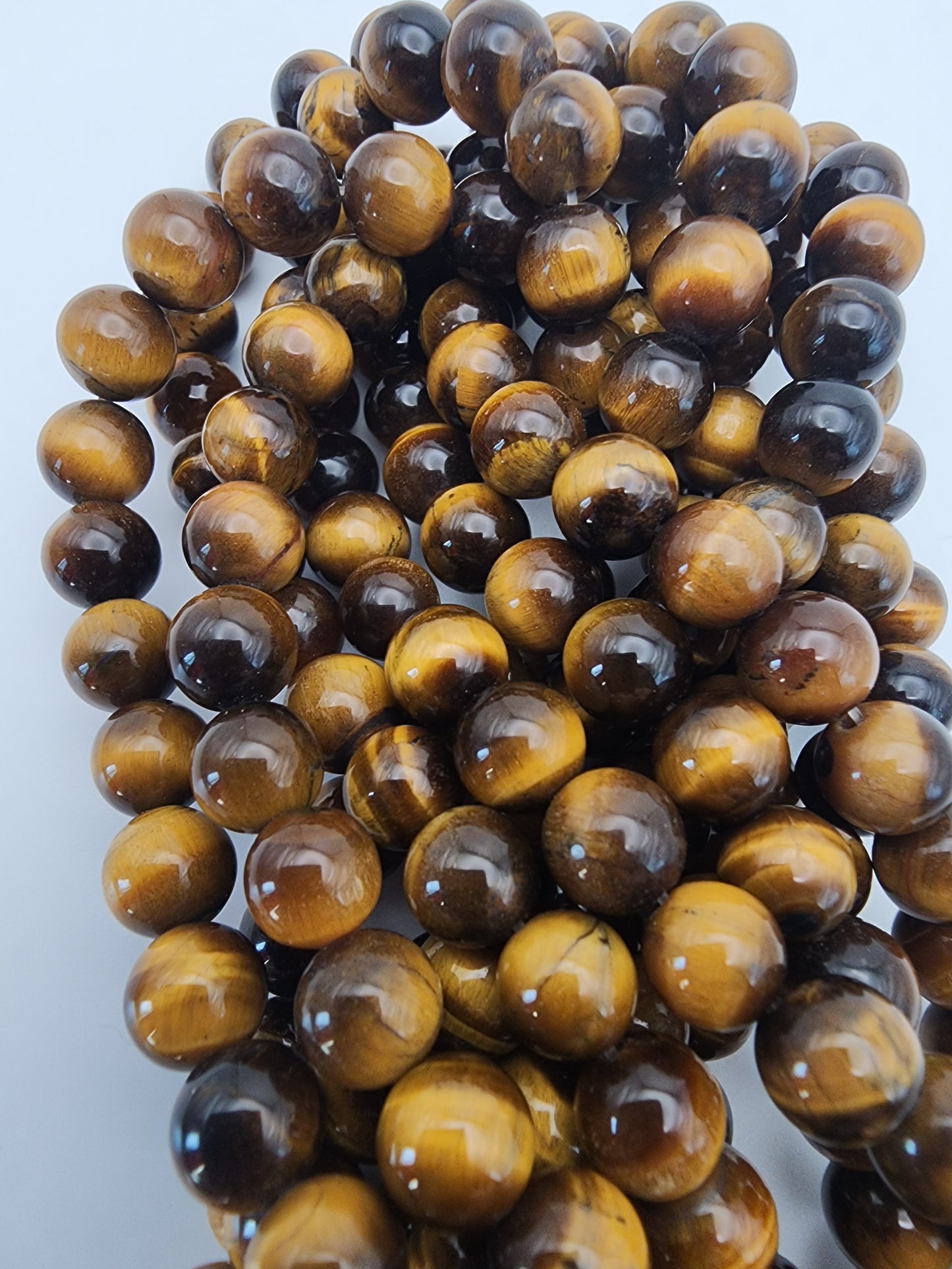 A close-up of the 8mm Tiger's Eye Round beads, highlighting their glossy surface and the rich amber and brown hues. The beads are grouped together, showcasing their smooth, round shape and distinctive banded patterns.
