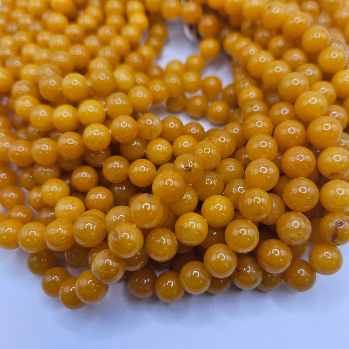 A close-up of multiple shiny 8mm Yellow Jade Round Bead Strands, featuring a smooth surface, delicately arranged on a light background.