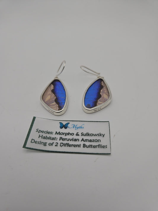 A pair of Sterling Silver Butterfly XL Tear Earrings showcases teardrop-shaped silver frames with vibrant blue butterfly wing patterns. A nearby label reads: "Species: Morpho & Sulkowsky, Habitat: Peruvian Amazon, Design of 2 Different Butterflies." These exquisite earrings embody the essence of second life jewelry.