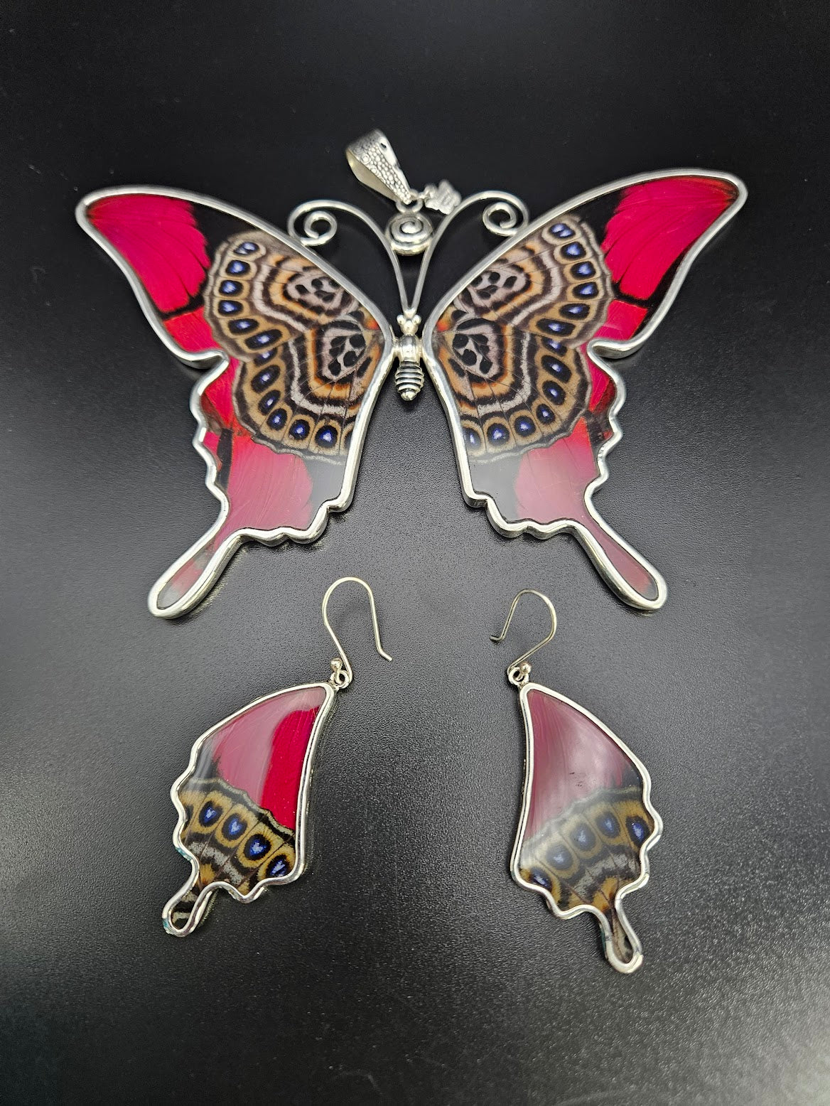 Discover the Sterling Silver Butterfly XXL Set, which includes a butterfly-shaped pendant and matching earrings adorned with vibrant red and intricate patterns against a striking black background. The design is highlighted by silver outlining, elevating the artistic details for expert-level performance in style.