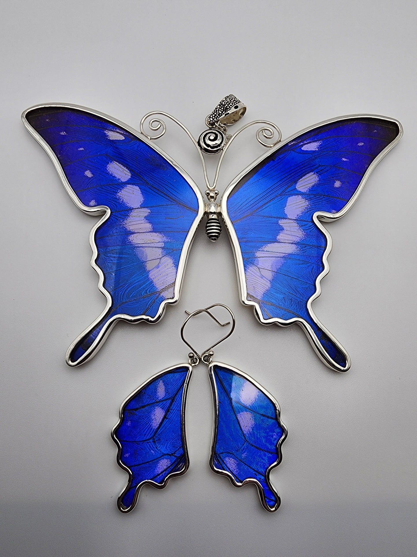Introducing the Sterling Silver Butterfly XXL Set: a stunning butterfly-shaped jewelry collection that exemplifies expert-level design. This set includes a large blue butterfly necklace with intricate silver detailing, accompanied by matching blue wing-shaped earrings, all elegantly showcased against a plain white background.