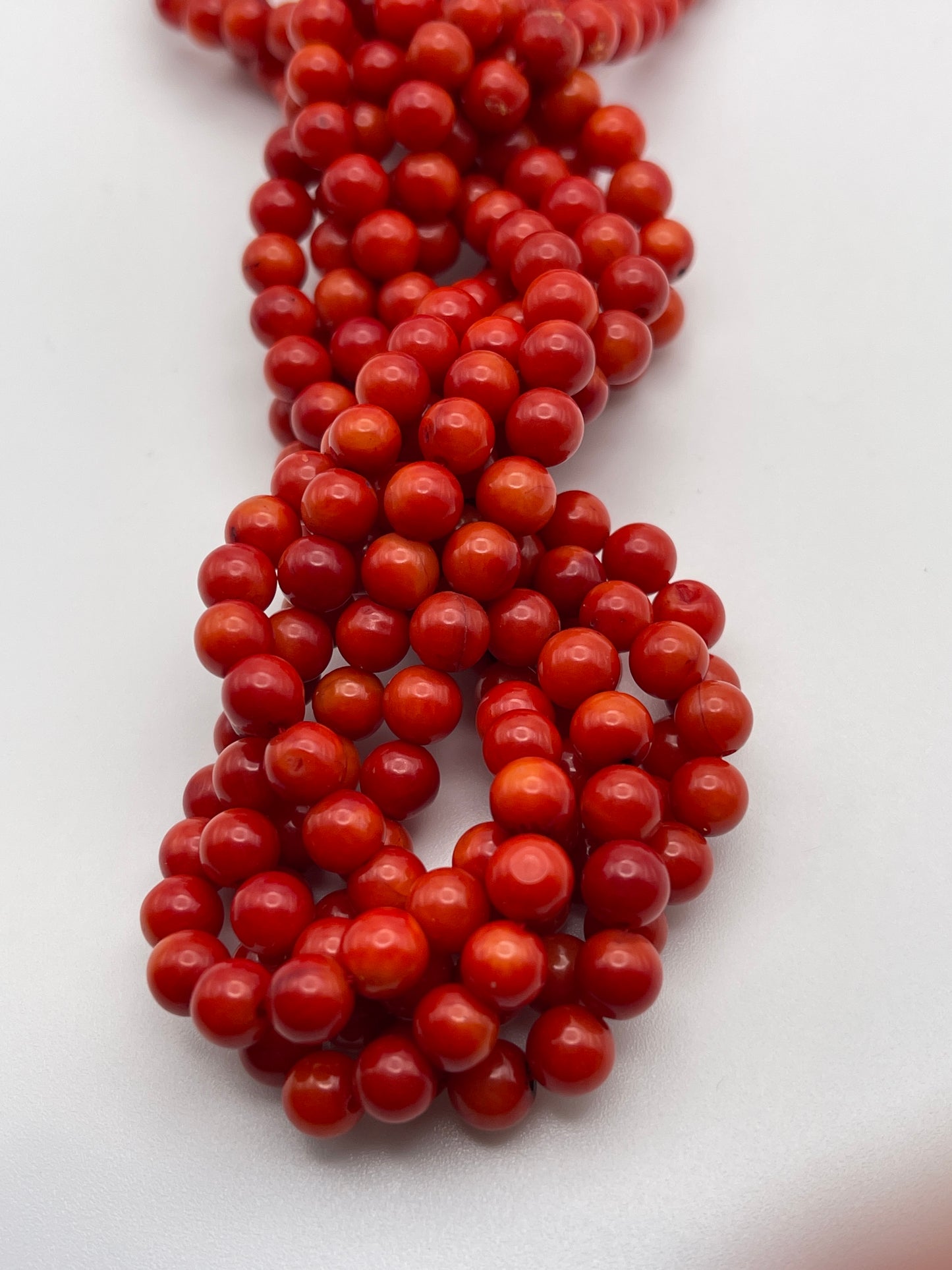 A close-up image of multiple intertwined strands of shiny, round, 6mm Coral beads set against a white background.