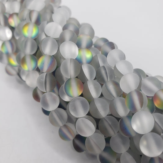 A close-up of 8mm White Matte Mermaid Glass beads with a subtle rainbow sheen. The spherical beads are closely packed, creating a shimmering effect against a plain white background.