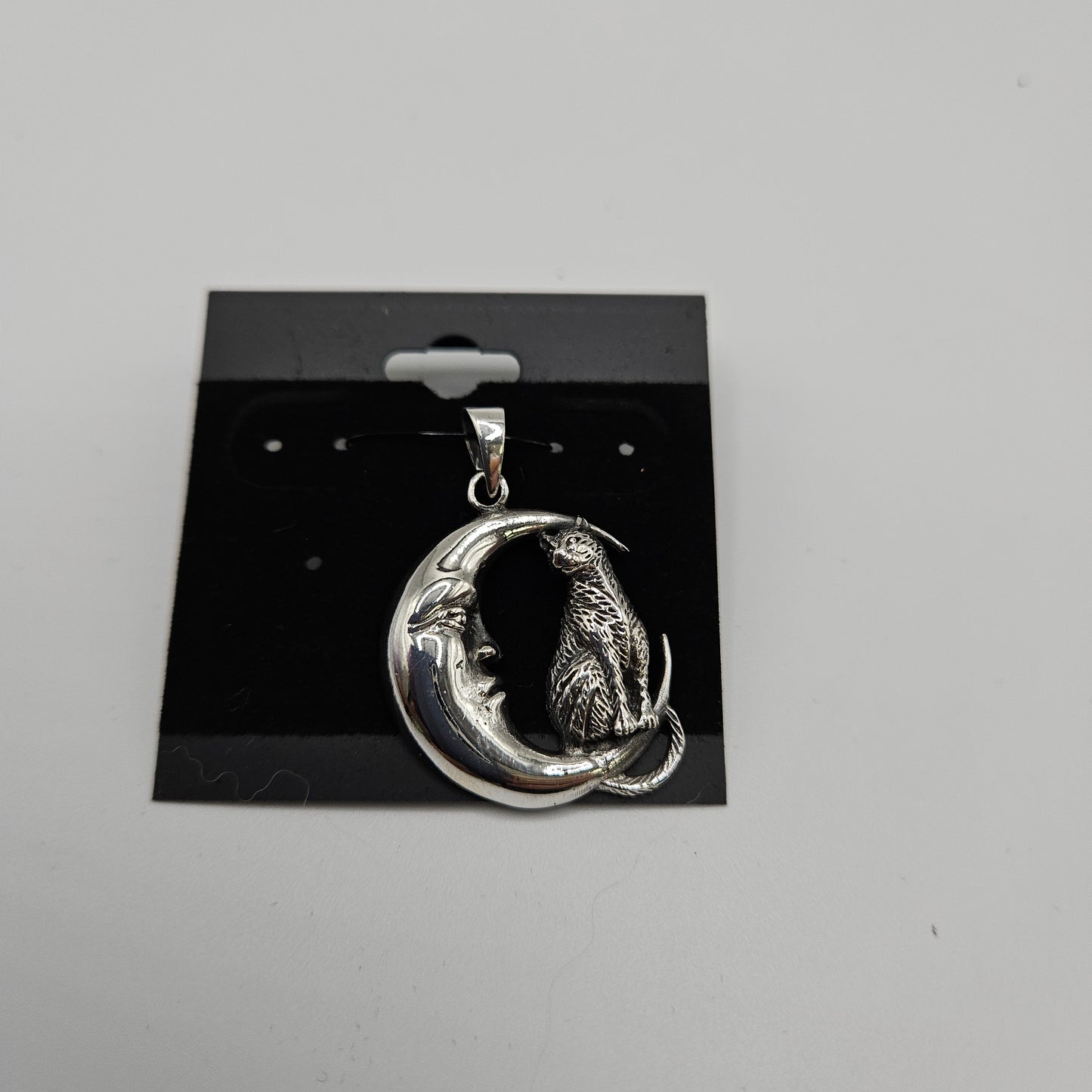 The SS Cat on Moon Pendant, priced at $44.99, displays a silver crescent moon with a face alongside a sitting cat, elegantly presented on a black card.