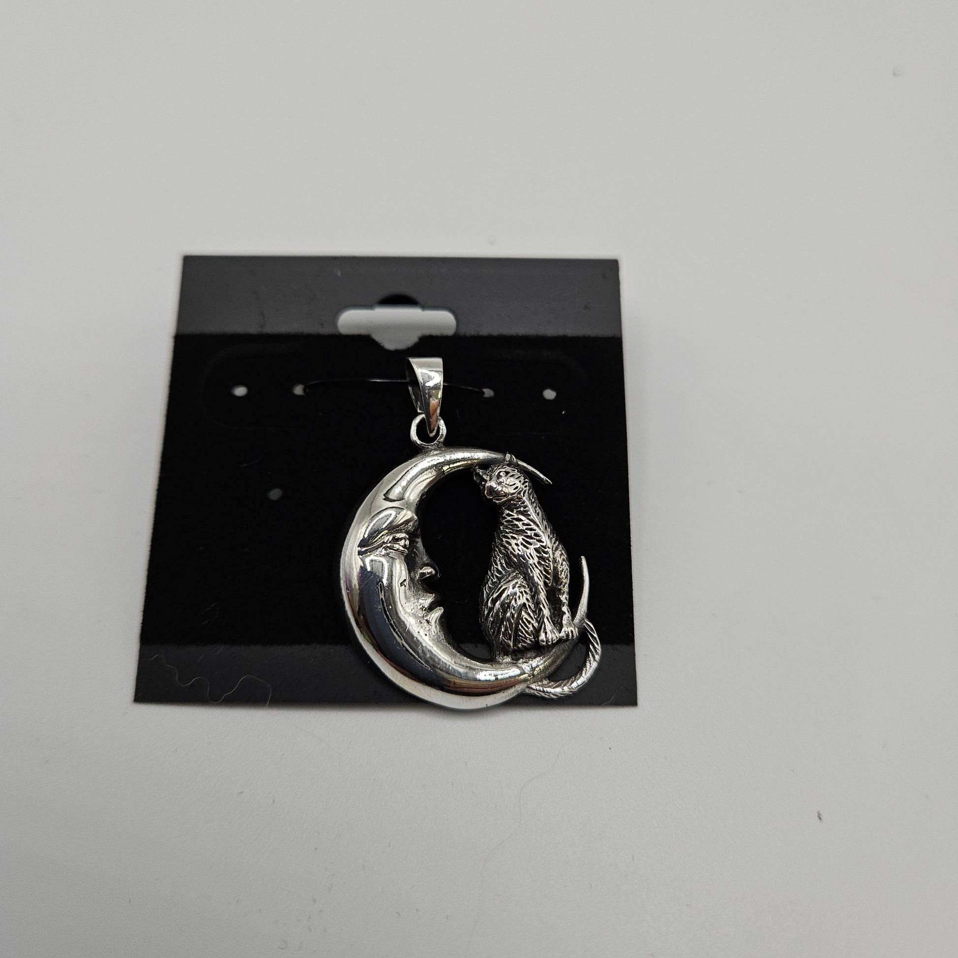 The SS Cat on Moon Pendant, priced at $44.99, displays a silver crescent moon with a face alongside a sitting cat, elegantly presented on a black card.