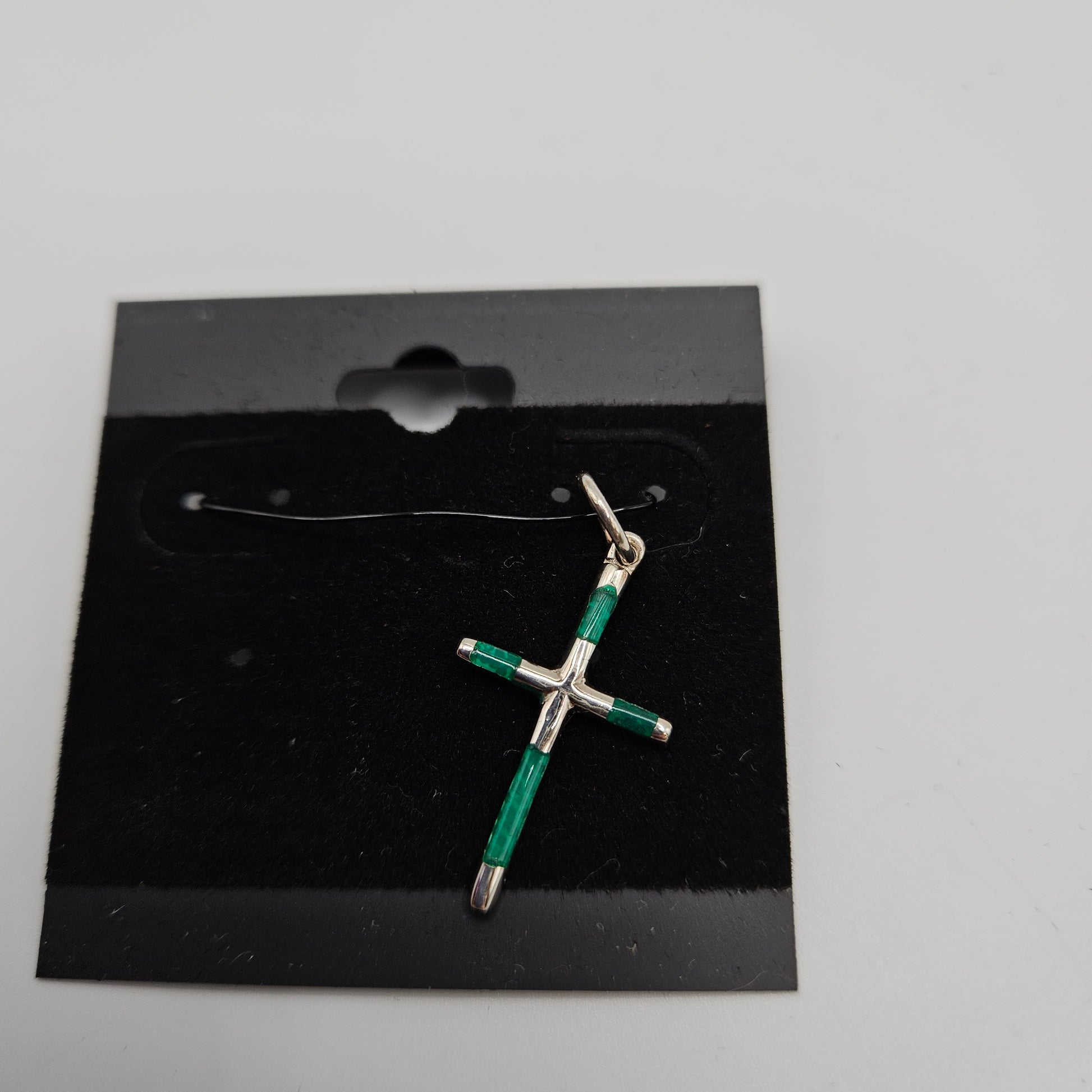 A green and silver cross pendant on a black card with a small silver chain