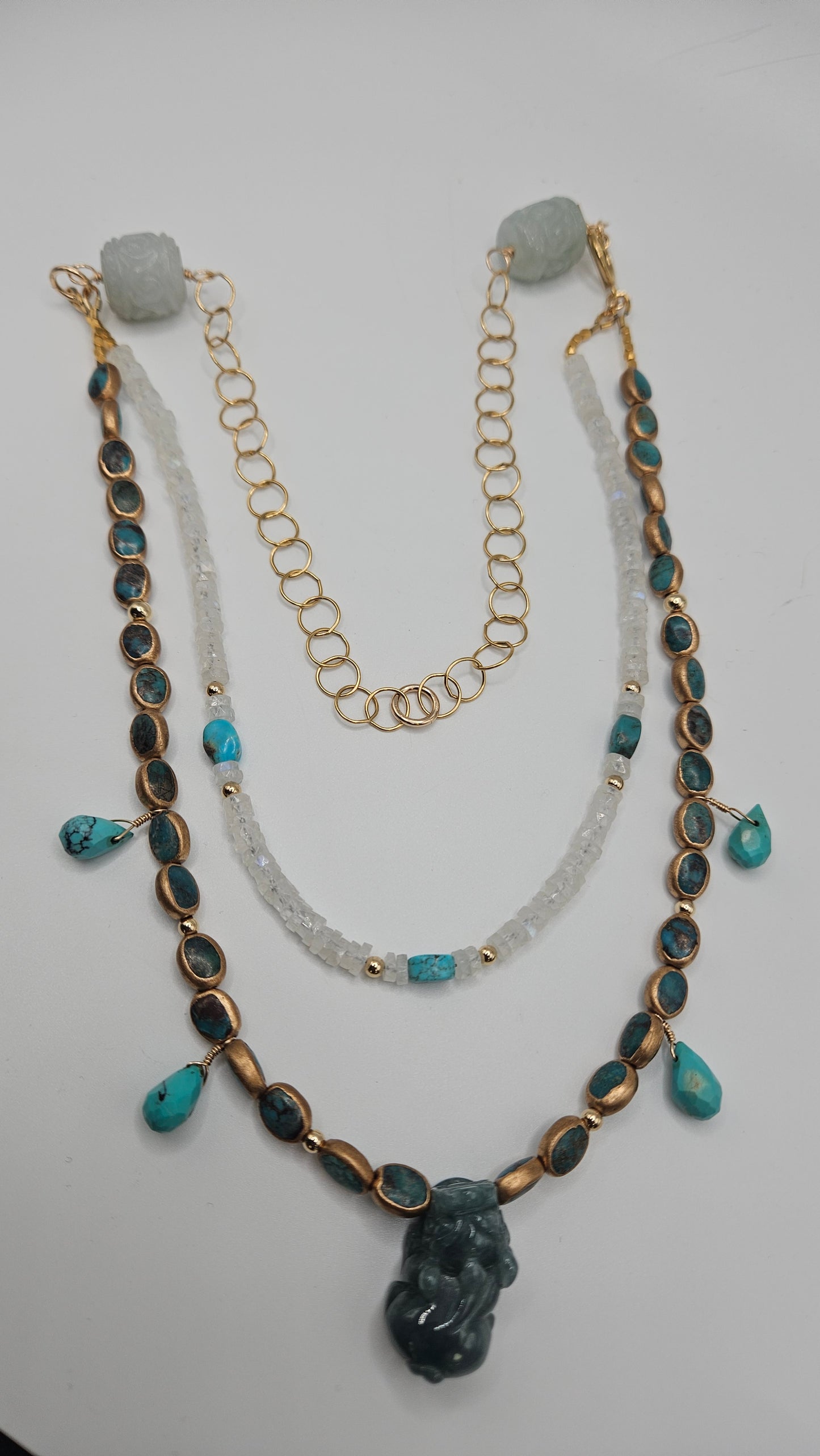 A multi-strand turquoise, moonstone, and jade dragon necklace with gold accents.