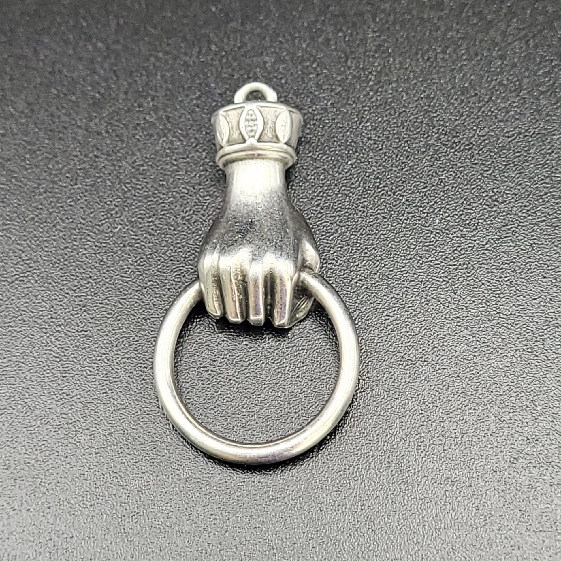 A silver-colored hand wrist ring charm with a small crown on top of the ring