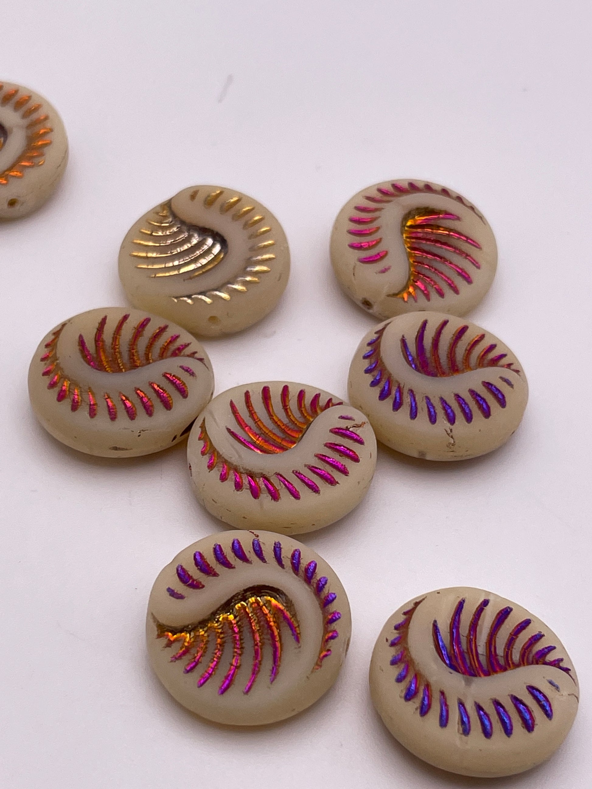  18mm White & Metallic Wave Czech Single Beads are scattered on a white surface, each showcasing colorful, metallic spiral grooves in vibrant shades of orange, purple, and pink against cream backgrounds to create a lively decorative pattern.