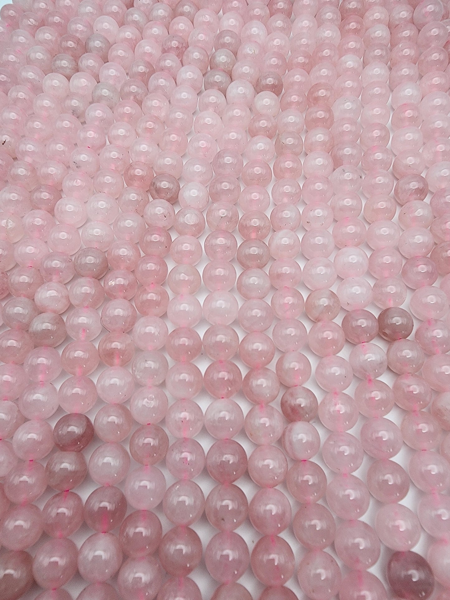 The 8mm Rose Madagascar Quartz Round beads are tightly arranged, forming a geometric and glossy texture. The spherical beads display slight variations in shade, spanning from light to medium pink, and they catch and reflect light beautifully.