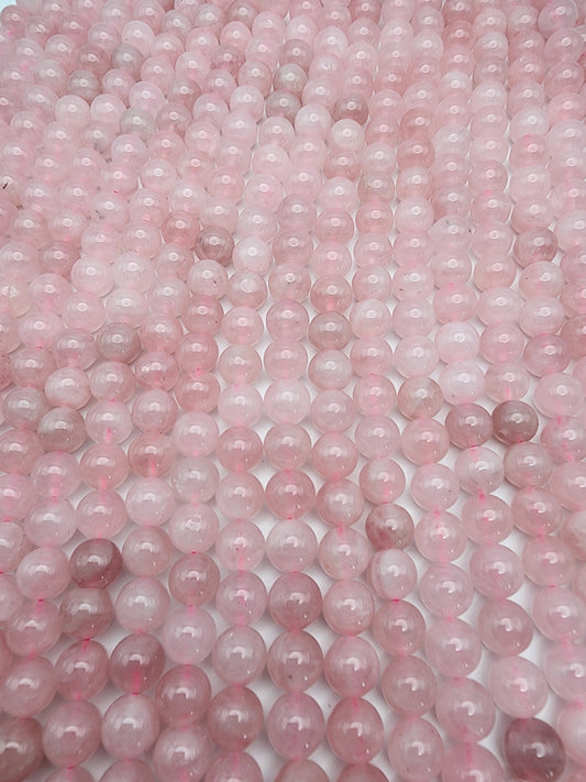 The 8mm Rose Madagascar Quartz Round beads are tightly arranged, forming a geometric and glossy texture. The spherical beads display slight variations in shade, spanning from light to medium pink, and they catch and reflect light beautifully.