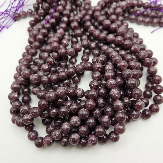 Close-up of several strands of 8mm Lepidolite round beads with speckles, arranged in loops on a white background. The beads have a shiny, polished surface, and the strands end with purple thread.