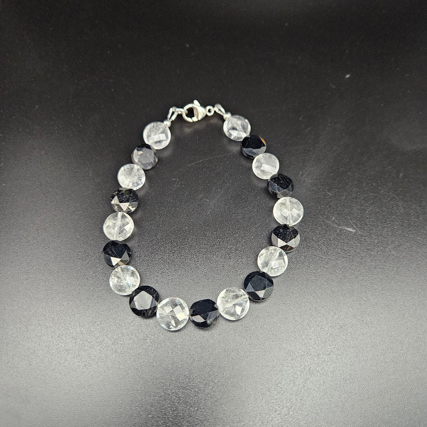 A black tourmaline and clear quartz coin bracelet with a silver-colored chain, 