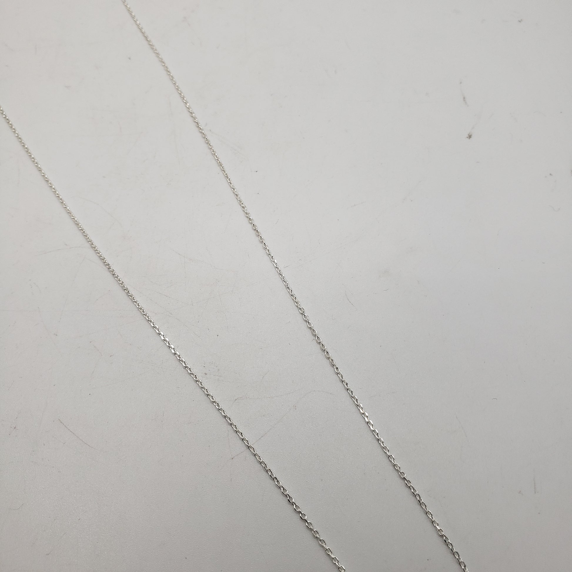 The 20 inch Sterling Silver Link Chain is elegantly displayed against a simple, light-colored background. Its fine link pattern runs diagonally across the image, exuding simplicity and grace.