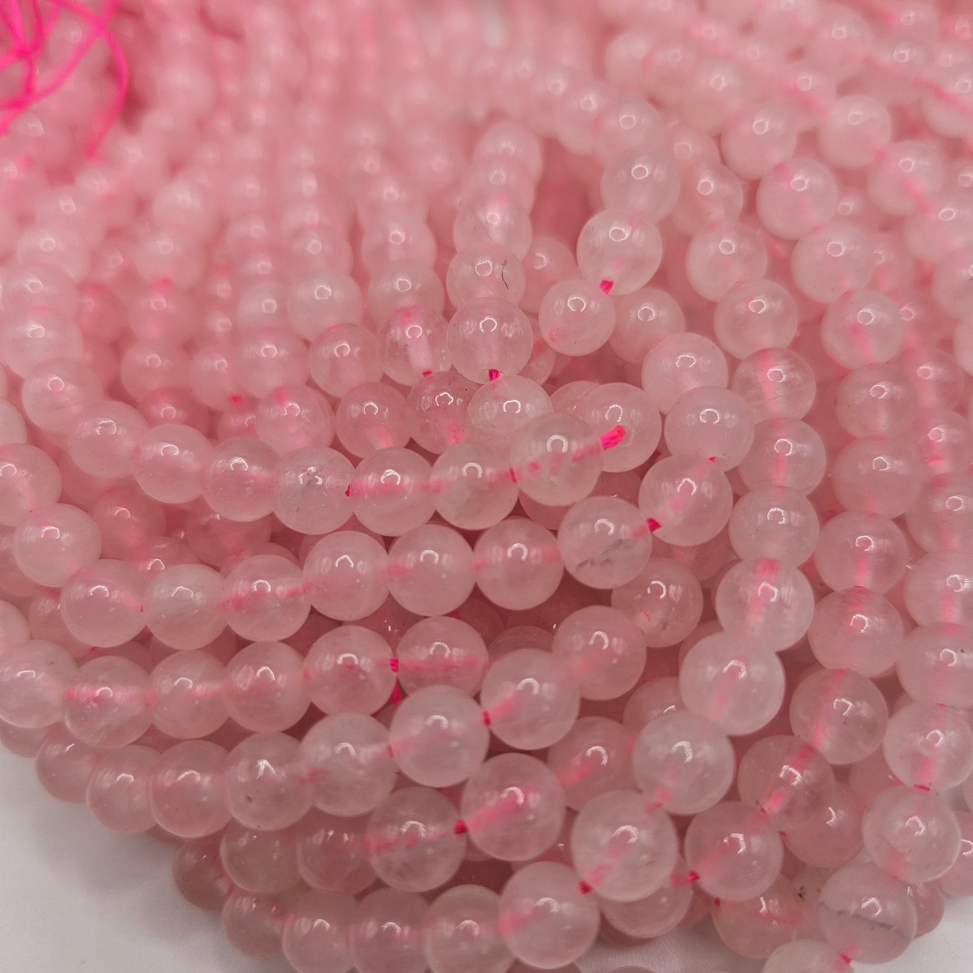 Close-up of 6mm Rose Quartz Round Bead Strands, featuring several strands of shiny beads strung together with pink thread.