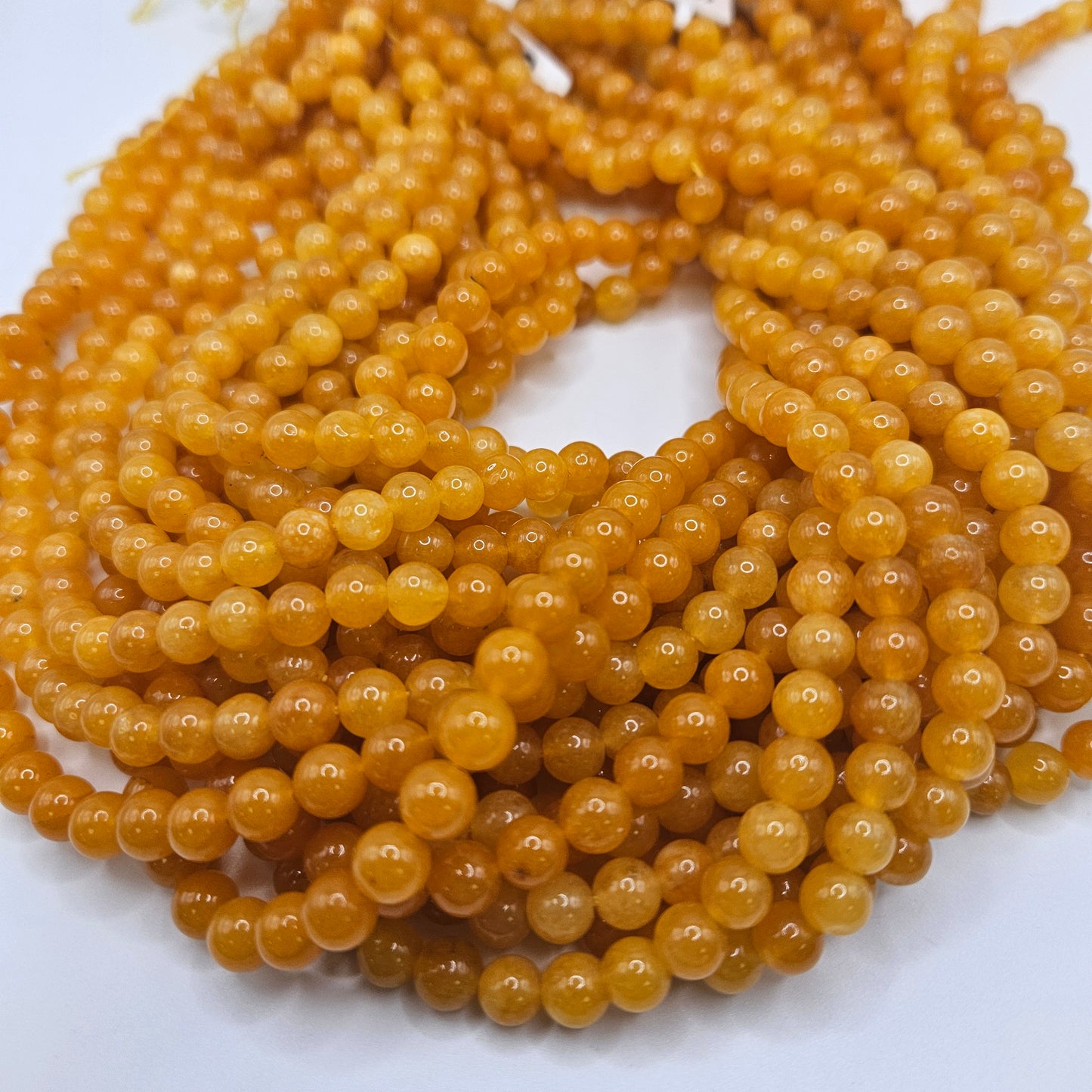 A close-up view showcases the smooth texture and warm hue of multiple strands from the 6mm Yellow Jade Round Bead Strand, accentuating their polished, honey-colored appearance.