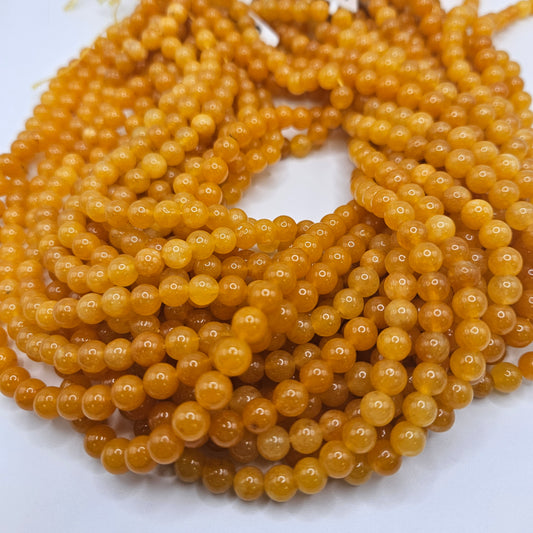 A close-up view showcases the smooth texture and warm hue of multiple strands from the 6mm Yellow Jade Round Bead Strand, accentuating their polished, honey-colored appearance.