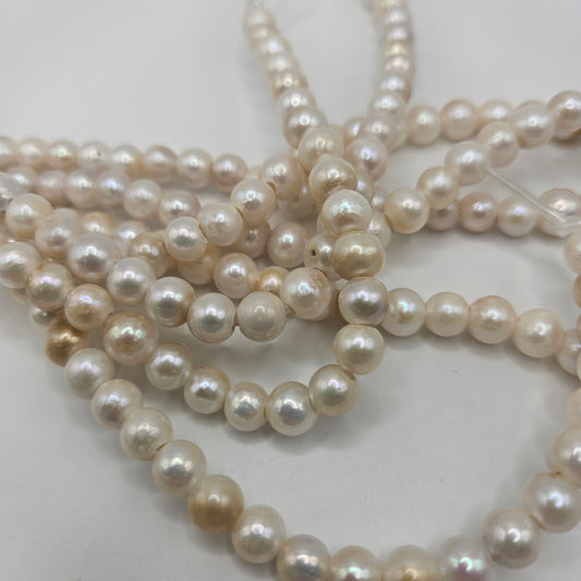 Close-up of several strands from the 8mm Freshwater Pearls Round Bead Strand in white and cream hues. These pearls are slightly irregular in shape and vary in luster, lying intertwined on a white surface.