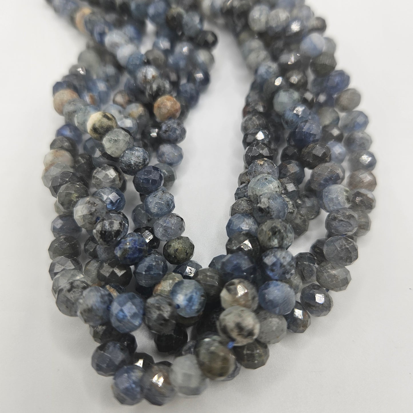 Close-up of 8mm Kyanite Faceted Rondelle Bead Strand, featuring blue beads with a marbled appearance in shades from dark to light blue on a white background.
