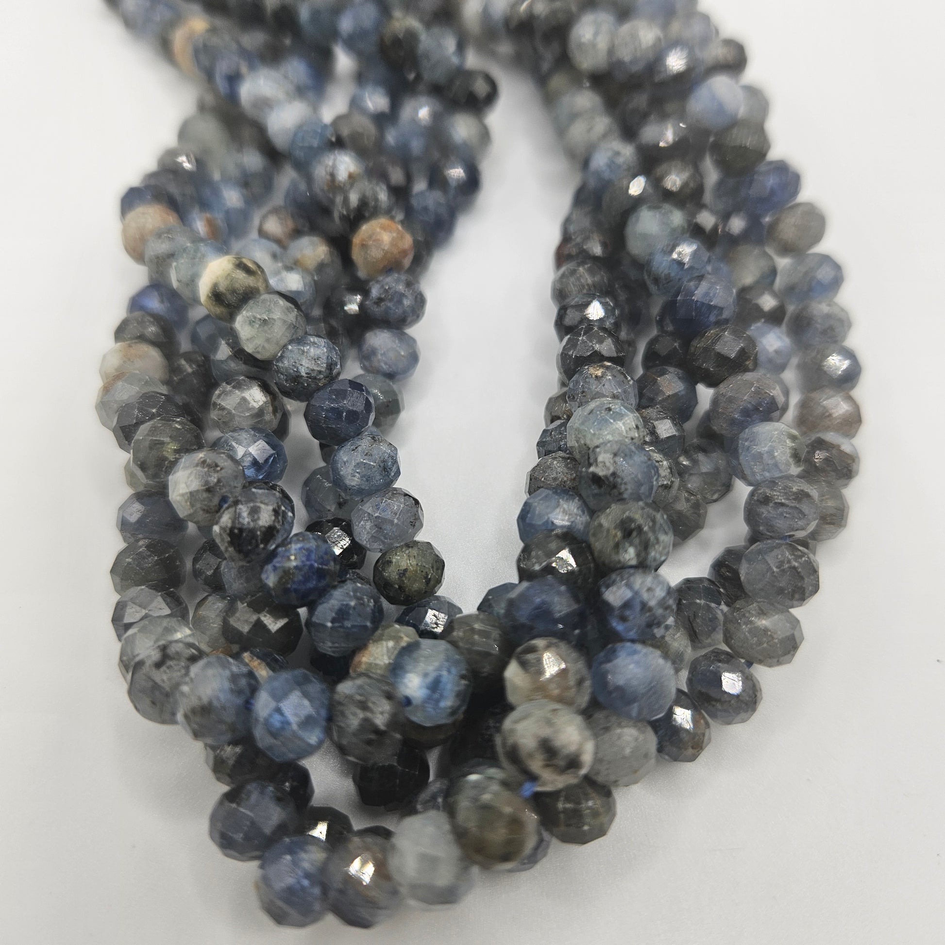 Close-up of 8mm Kyanite Faceted Rondelle Bead Strand, featuring blue beads with a marbled appearance in shades from dark to light blue on a white background.