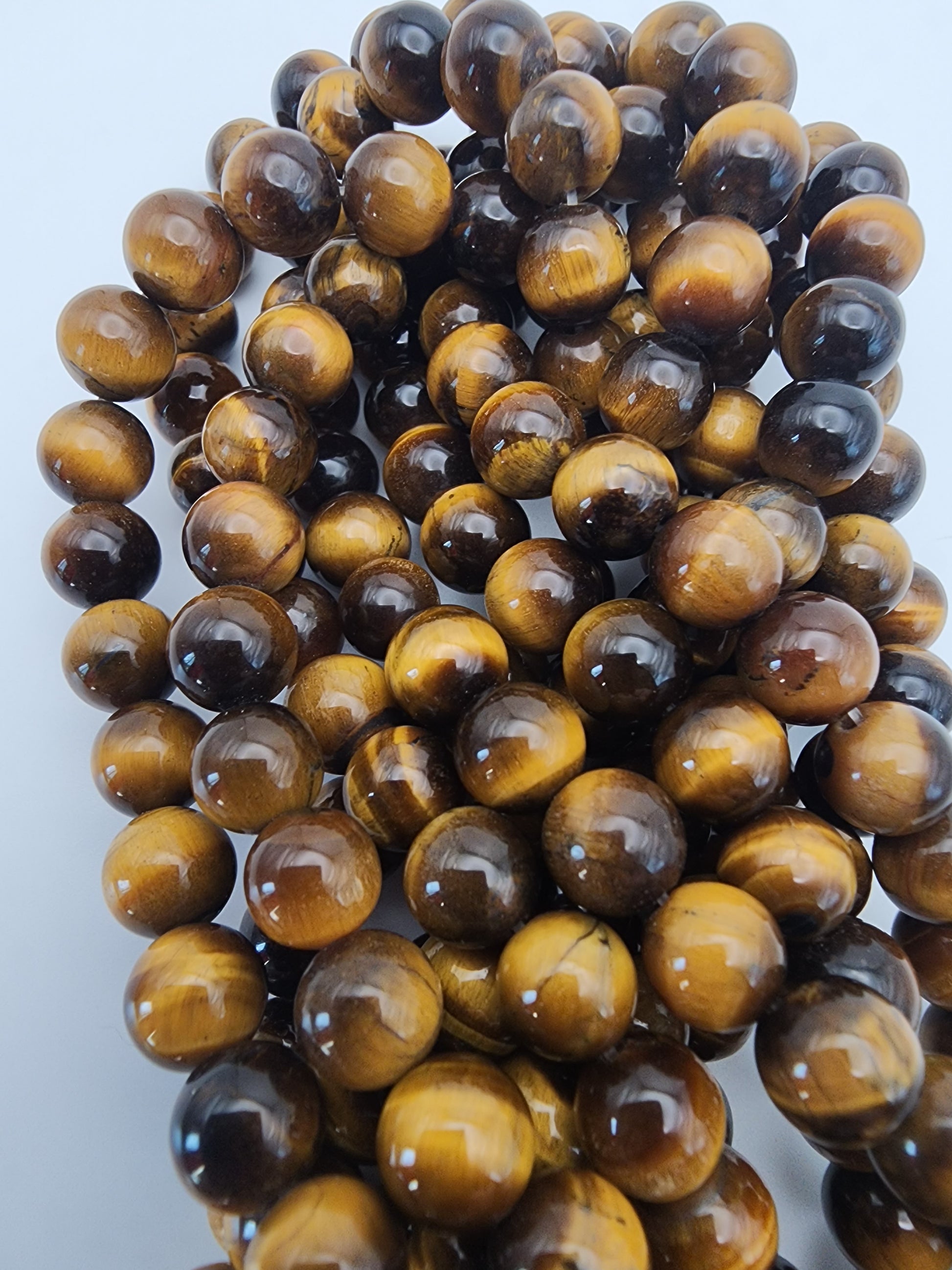 A close-up of the 8mm Tiger's Eye Round beads, highlighting their glossy surface and the rich amber and brown hues. The beads are grouped together, showcasing their smooth, round shape and distinctive banded patterns.