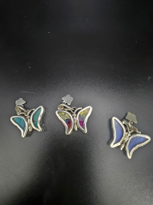 Three Sterling Silver Baby Butterfly Pendants, true pieces of butterfly jewelry art, showcase vibrant wings against a black background. Each pendant captures the essence of a butterfly sanctuary with distinct colors: green, red, and blue, all elegantly bordered by a silver outline.