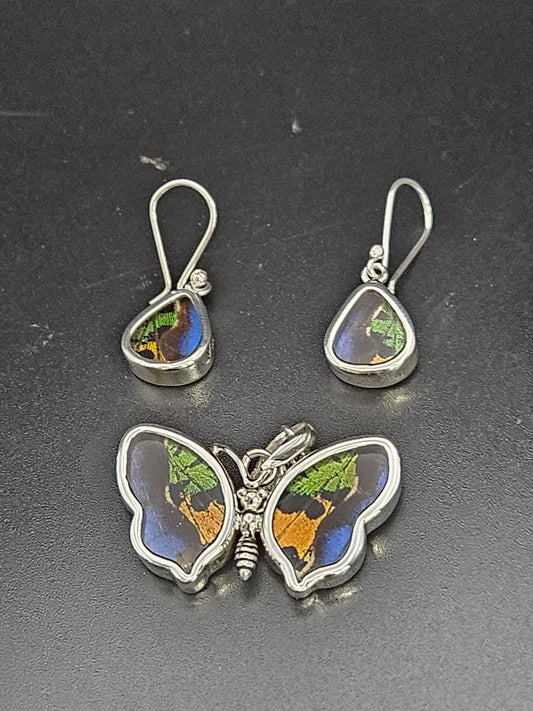 The Sterling Silver XL Butterfly and Wing Set consists of a butterfly-shaped pendant and teardrop earrings with vivid green, blue, and brown patterns on a black background, capturing the enchanting hues one might find in a butterfly sanctuary.